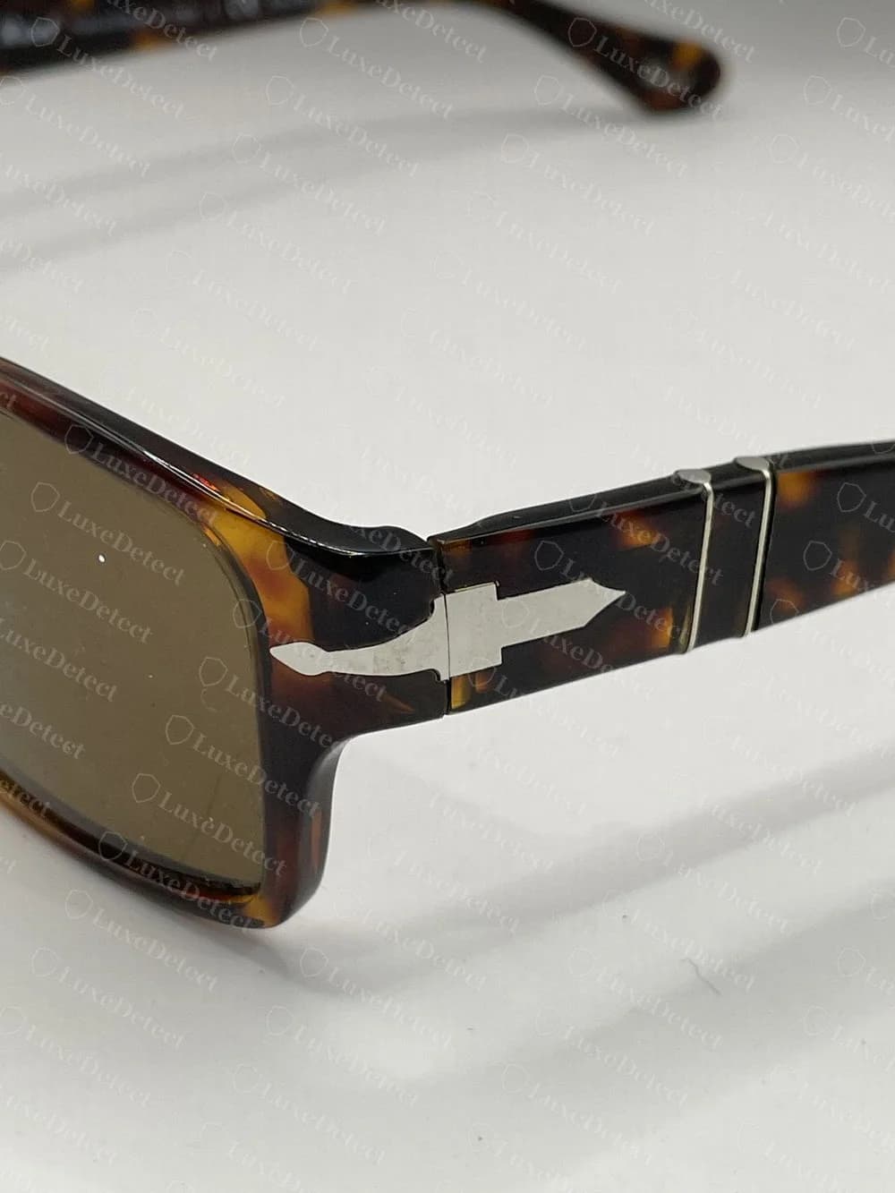 Dobradiça em flecha do Persol 2803-S original, uma flecha prateada rente ao acetato tartaruga, com duas finas barras de metal atravessando a haste logo atrás