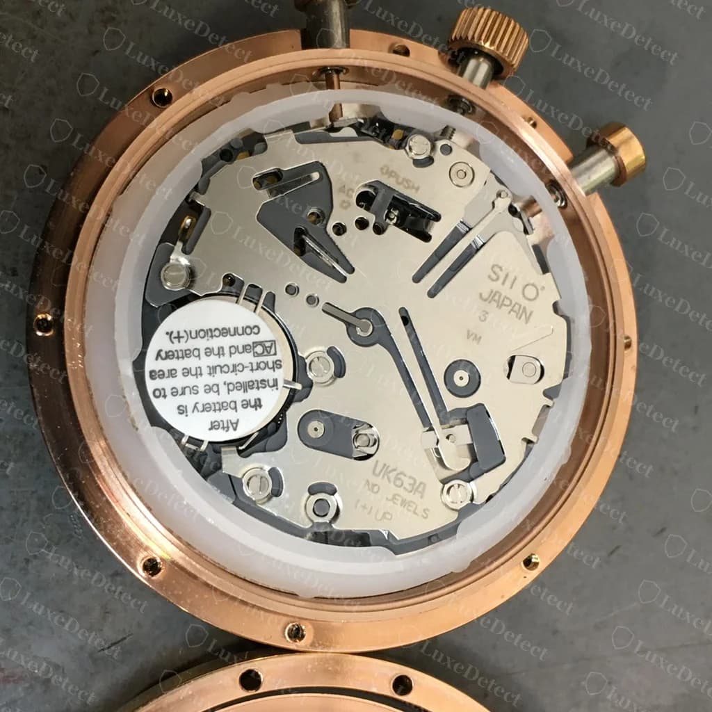 The same fake chronograph opened up: a Japanese quartz module stamped "SII O JAPAN... UK63A... NO JEWELS" with a coin-cell battery, nothing like the jewelled movement the caseback claims.