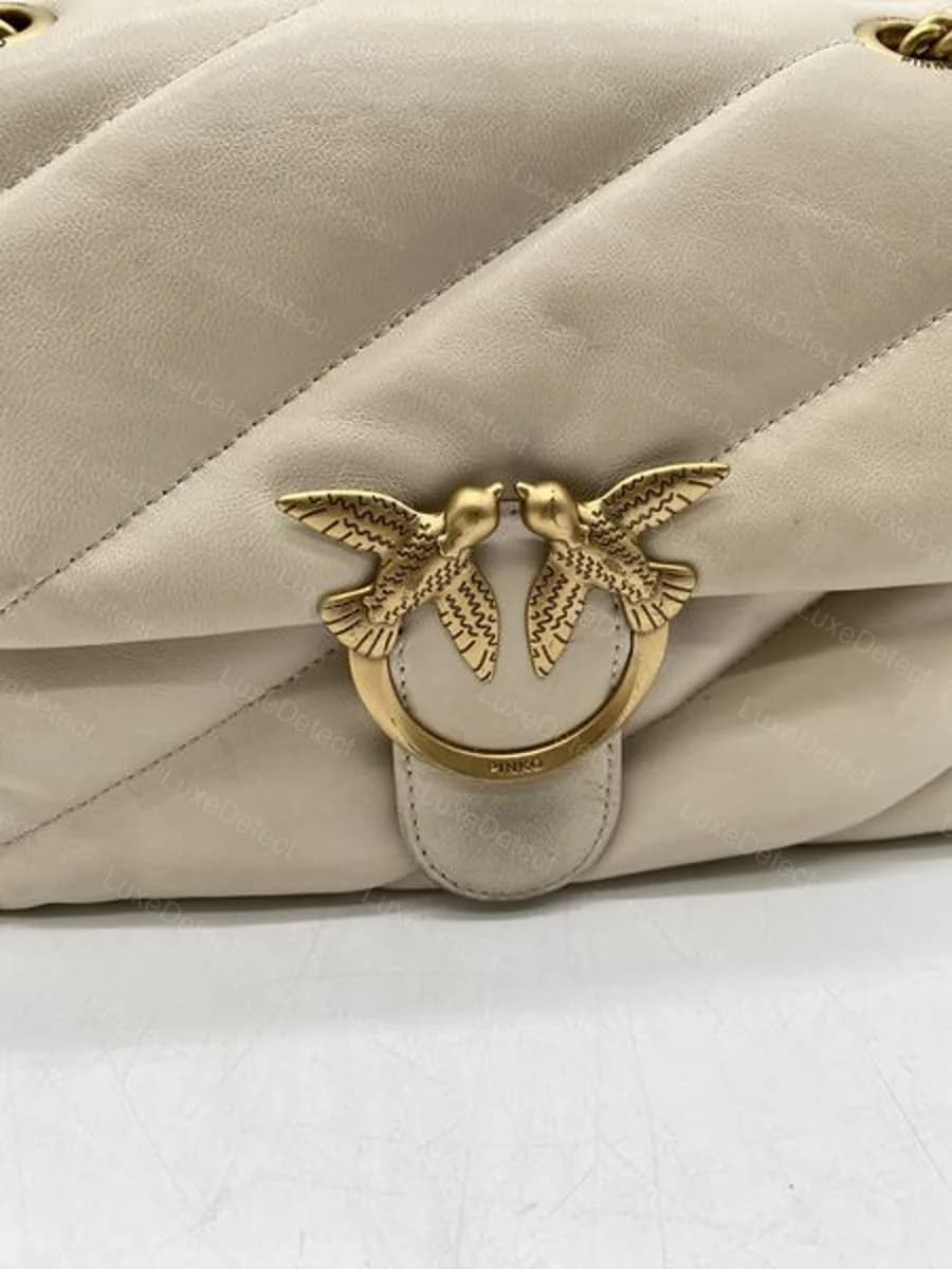Counterfeit Pinko Love Bag clasp (Puff variant), feather line-work and ring text detailed enough that the clasp alone does not separate it from a genuine bag