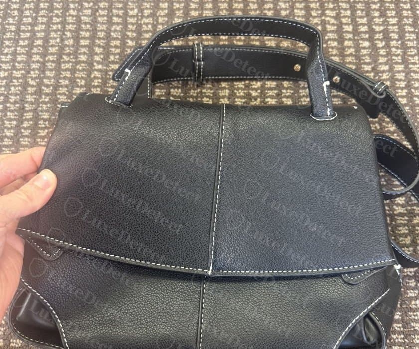 Aba frontal de uma falsificação da mesma silhueta: uma costura vertical visível desce pelo centro da aba e do corpo, o que o painel único da bolsa original não tem