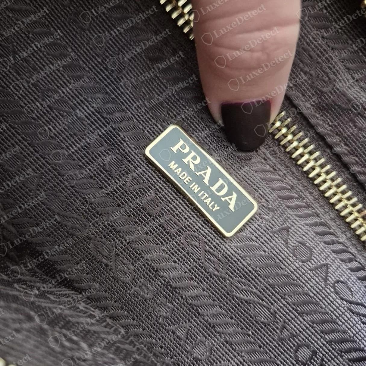 Gefälschte Prada-Schultertasche aus Veloursleder: dieselbe Aufschrift "PRADA MADE IN ITALY" auf einer Emaille-Plakette mit goldenem Rand über einem Logo-Jacquardfutter. Die Plakette selbst ist eine überzeugende Kopie