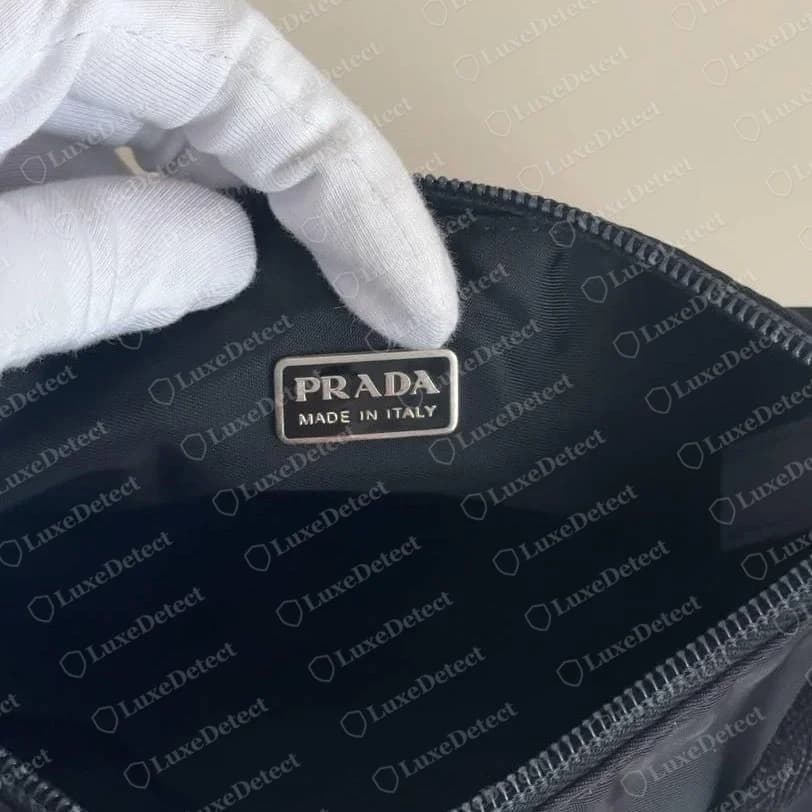 Pochette de nylon Prada original: placa metálica com os dizeres “PRADA MADE IN ITALY”, borda prateada, esmalte preto, costurada plana ao forro de nylon