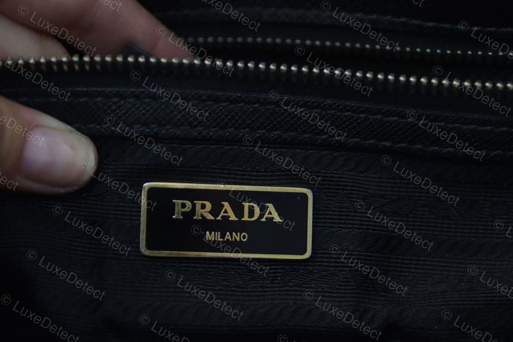 Authentic Prada interior — a metal enamel plaque reading "PRADA MILANO" set into the saffiano lining above the zip, gold foil on black enamel