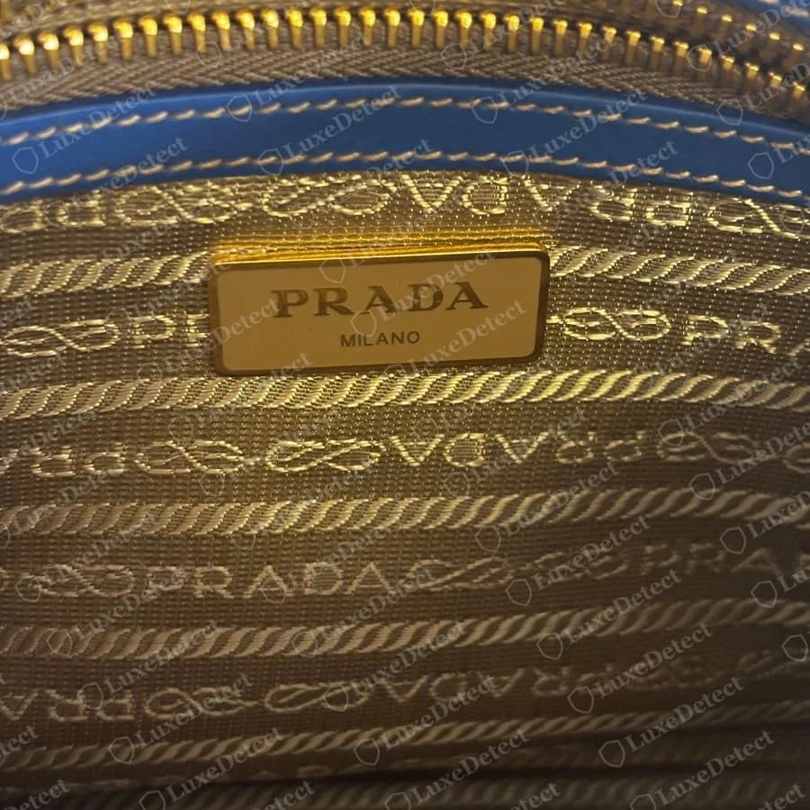 Echte Prada-Umhängetasche: Logo-Jacquardfutter mit Seilbändern und "PRADA"-Schriftzug in waagerechten Reihen, hinter einer cremefarbenen Emaille-Plakette "PRADA MILANO"
