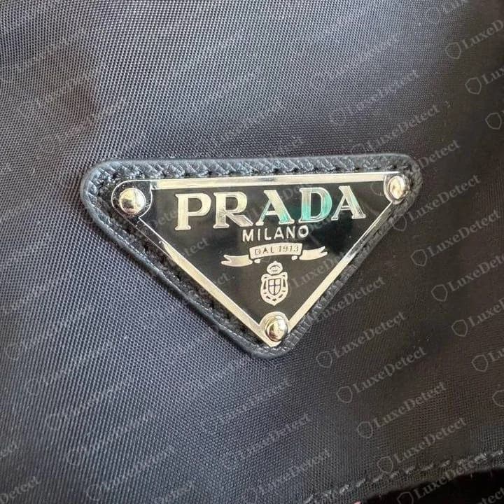 Gefälschte Prada-Messenger-Tasche aus Nylon mit Nieten: Das Dreieck ist scharf, und R, Abstand bei "DAL 1913" und Wappen sehen richtig aus, weshalb diese Plakette allein die Tasche nicht entlasten konnte