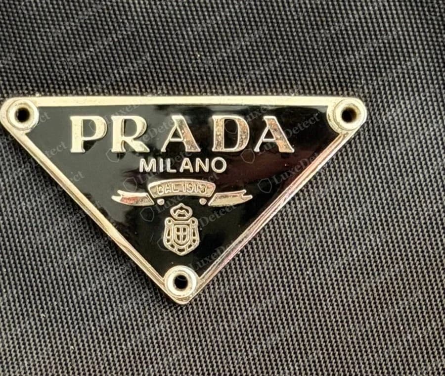 Pochette Prada Tessuto en nylon authentique : triangle émaillé noir au jambage du R incurvé, « MILANO », ruban « DAL 1913 » espacé et blason, fixé aux trois coins