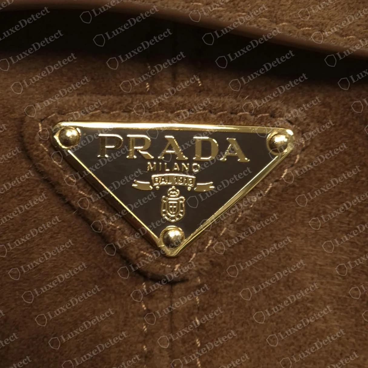 Faux sac Prada en daim porté épaule : un second faux avec un triangle doré net, un jambage du R incurvé et un émail assorti au daim marron