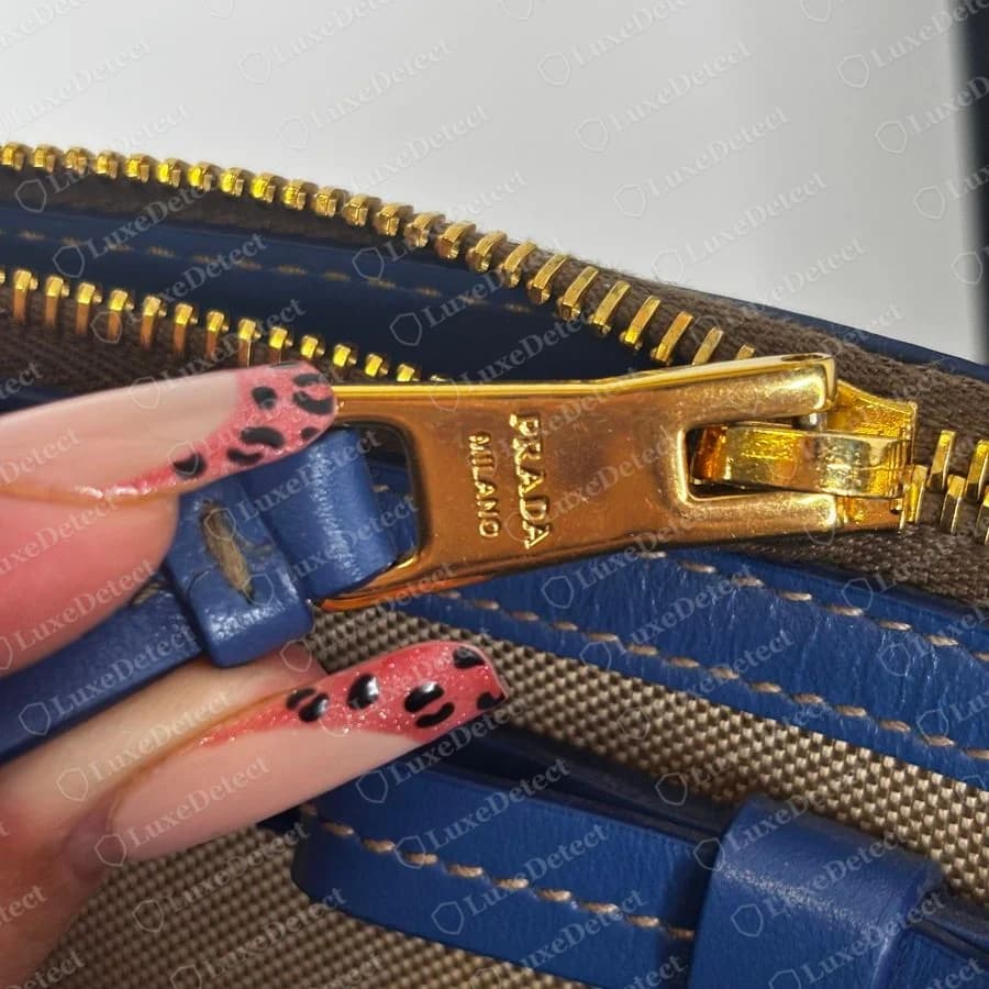 Bolsa transversal Prada original: puxador de zíper dourado com “PRADA MILANO” gravado com nitidez ao longo da lingueta, no mesmo tom dourado dos dentes e do cursor