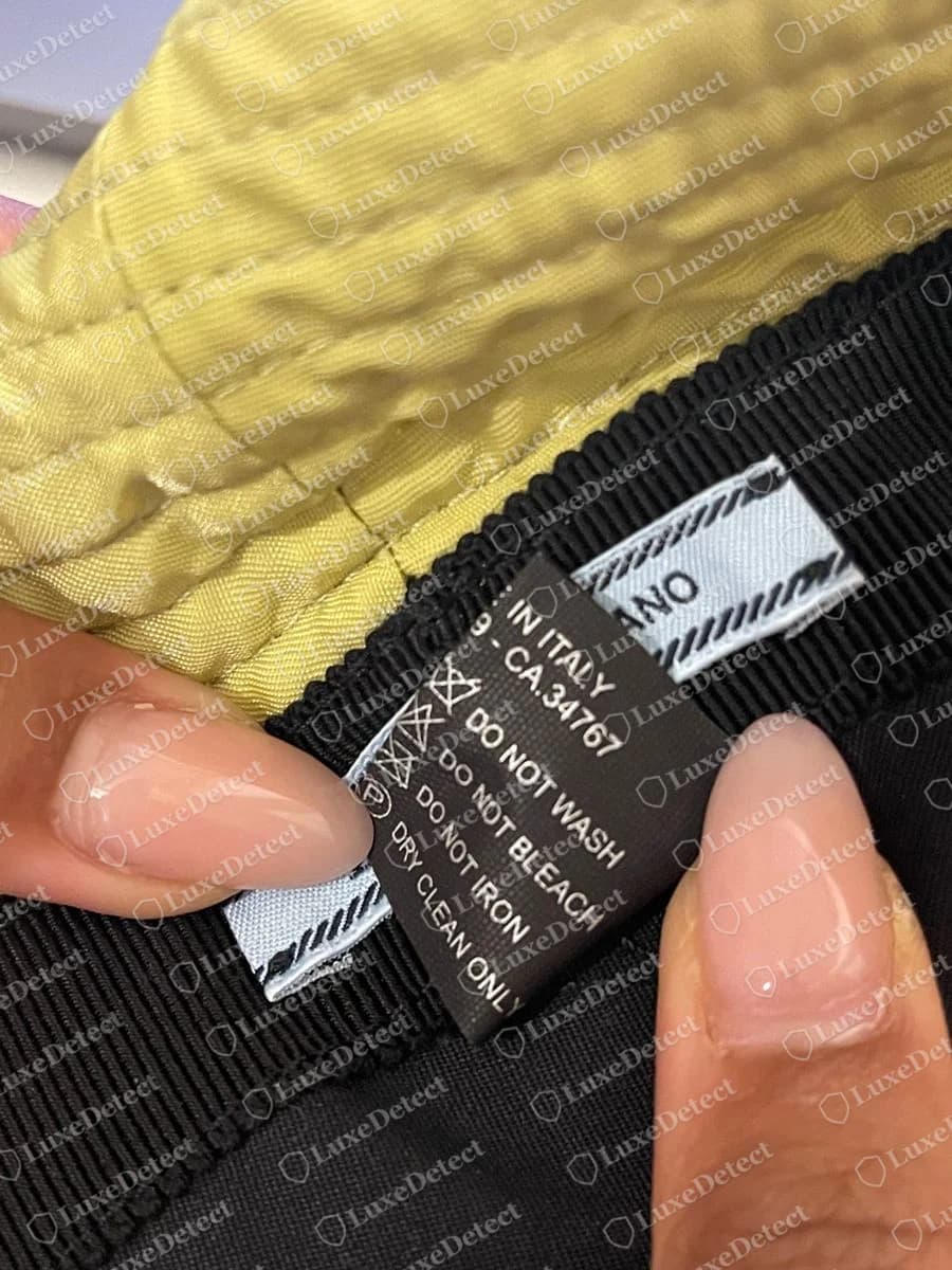 Etichetta di manutenzione di un bucket hat Prada originale più vecchio con IN ITALY, CA.34767, DO NOT WASH, DO NOT BLEACH, DO NOT IRON e DRY CLEAN ONLY accanto al nastro azzurro chiaro PRADA - MILANO