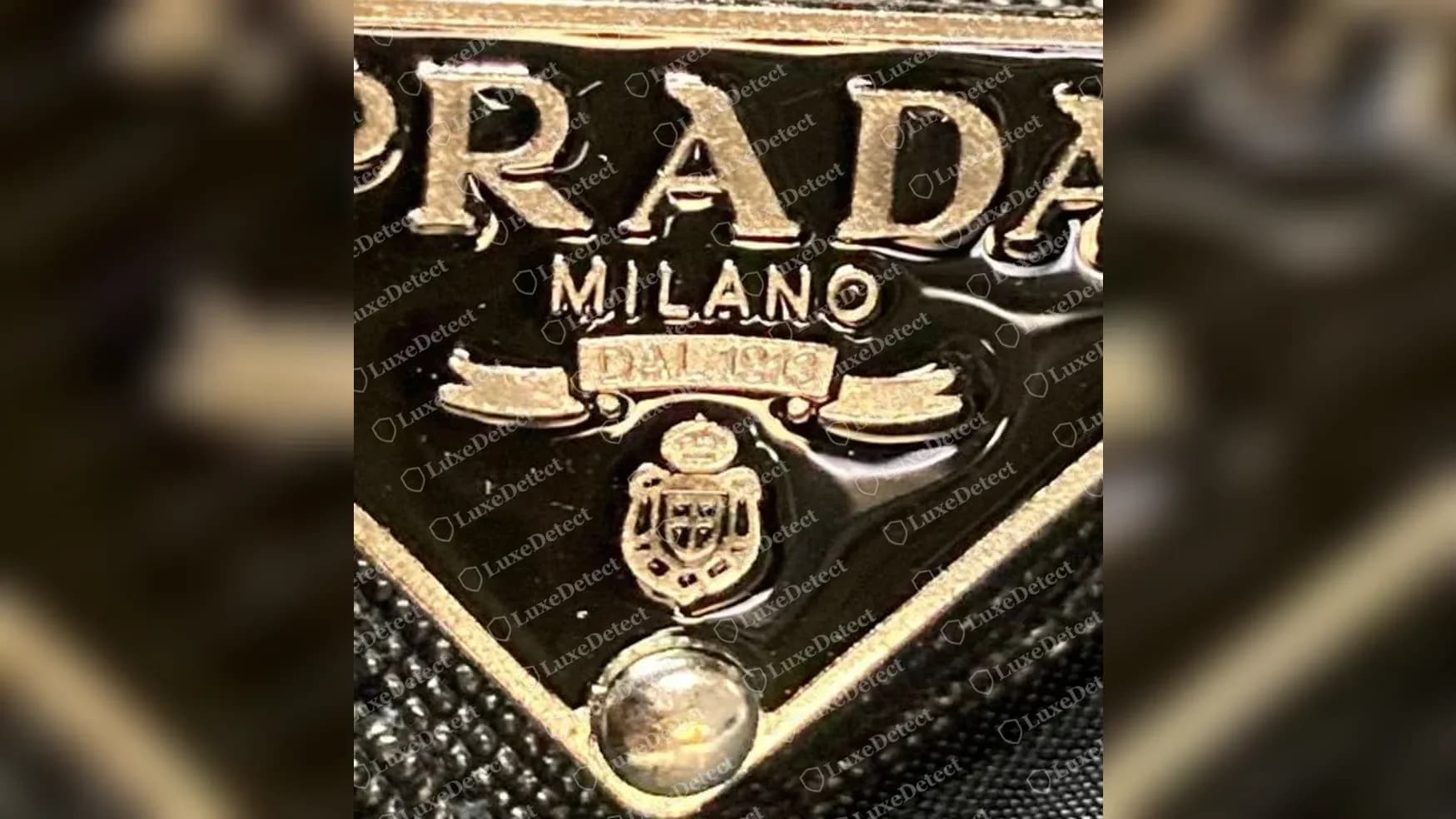 Primo piano della placca di un bucket hat Prada falso: lettere PRADA in rilievo irregolari, un nastro DAL 1913 sfocato e uno stemma irregolare
