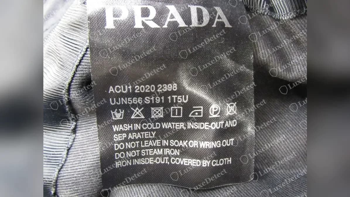 Etiqueta de cuidado de un gorro bucket hat Prada falso: un logotipo PRADA grande sobre los códigos ACU1 2020 2398 y UJN566 S191 1T5U, con instrucciones de lavado en inglés que incluyen las erratas SEP ARATELY e INISDE-OUT