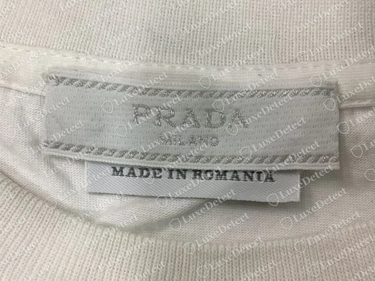 Halsetikett eines echten Prada T-Shirts: „PRADA / MILANO“ gewebt zwischen diagonal gestreiften Rändern, mit einem separaten Streifen „MADE IN ROMANIA“ darunter.