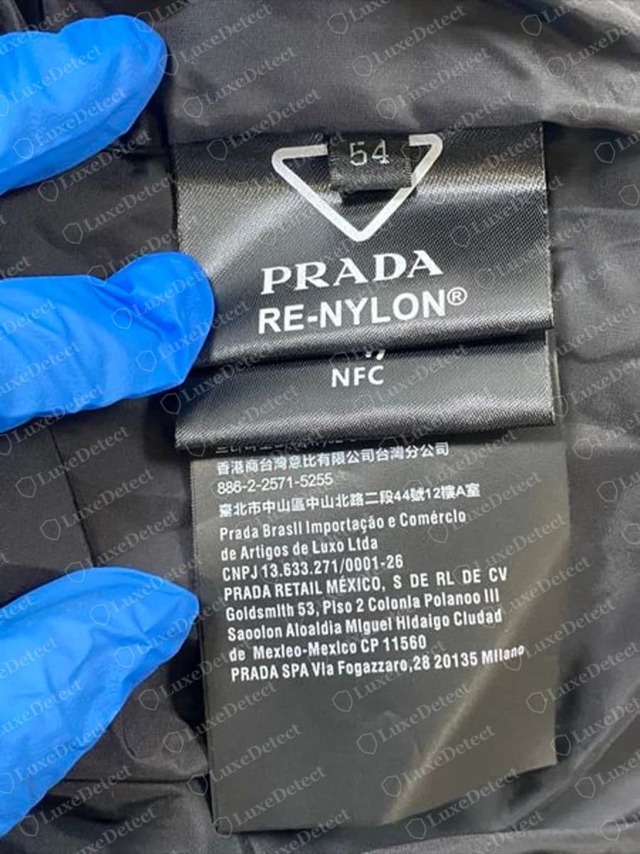 Etiqueta de una chaqueta Prada Re-Nylon genuina: triángulo de flecha con la talla dentro, "PRADA RE-NYLON®" con el signo de registro, un panel NFC y luego el bloque de importadores.