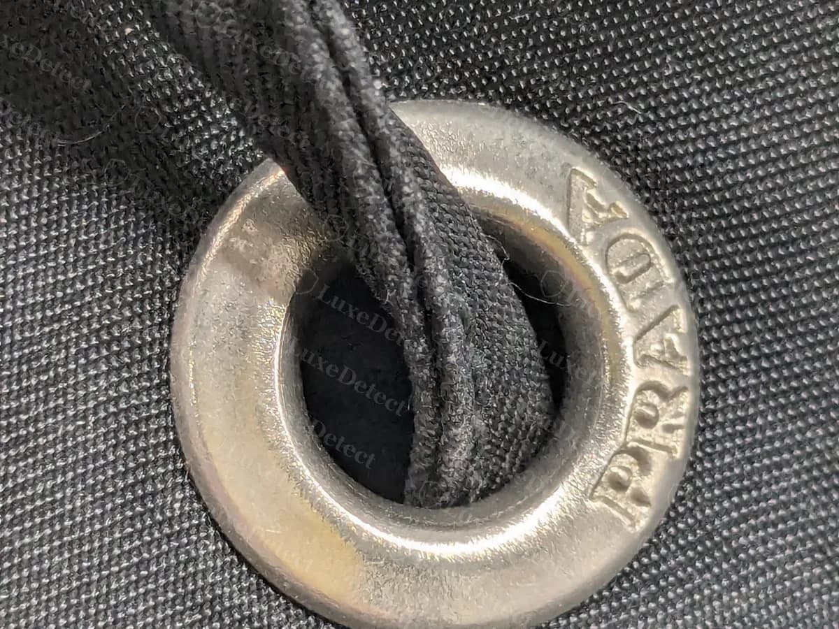 Genuine Prada backpack drawstring eyelet: a thick silver-tone ring around the cord hole, with PRADA stamped into the metal
