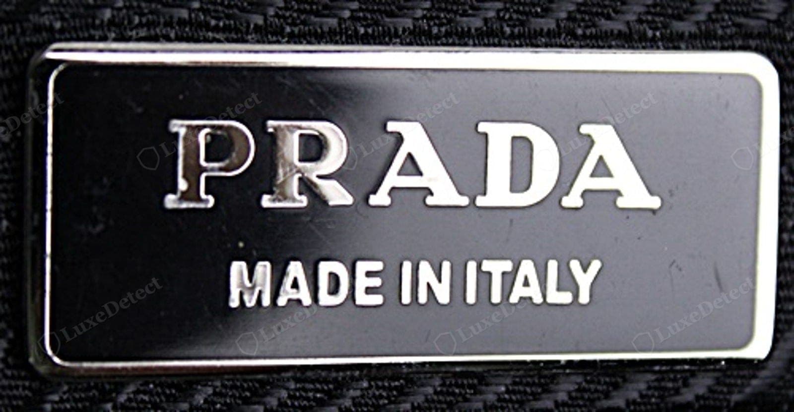 Counterfeit Prada Re-Edition metal plaque — faintly furry "PRADA" lettering, domed or matte enamel, a plaque that lifts at a corner