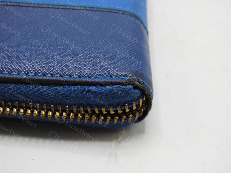 Zipper corner edge finishing on a counterfeit Prada wallet — cracked, lifted edge paint exposing frayed woven fiber underneath
