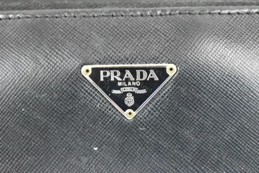 Prada triangle logo plaque, counterfeit — closely matches the authentic plaque's construction and text quality