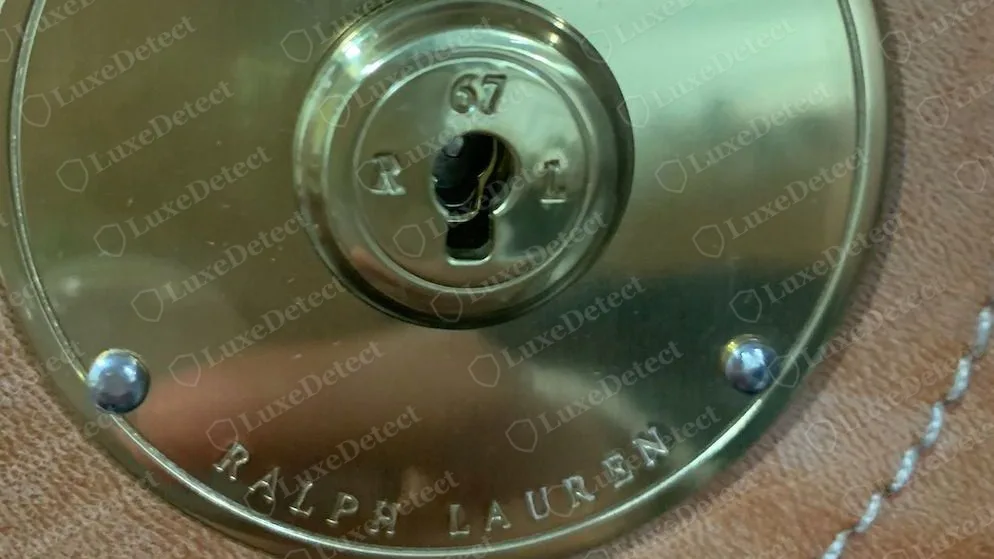 Cierre Ricky de Ralph Lauren genuino: placa redonda pulida sujeta con tornillos, el cilindro de la llave grabado con 67 sobre R y L, y RALPH LAUREN grabado alrededor del borde inferior