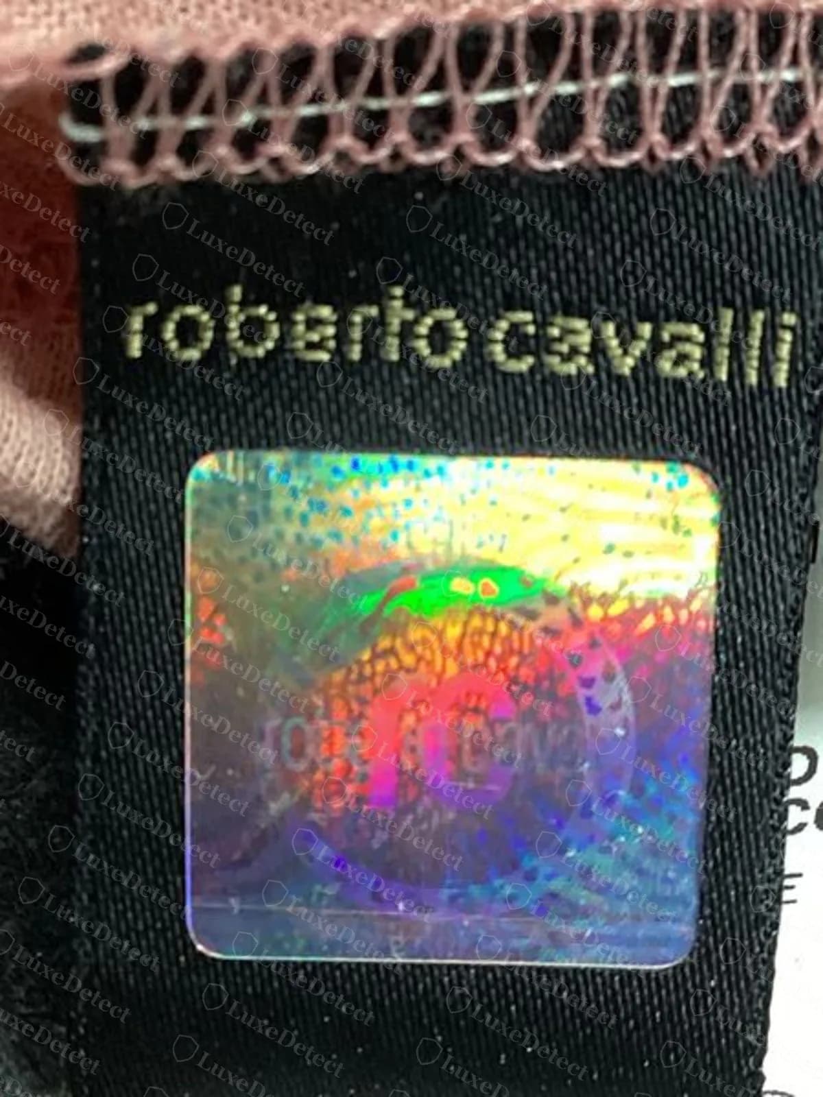 Lengüeta negra con holograma de Roberto Cavalli original, con roberto cavalli en letras doradas sobre un rectángulo holográfico arcoíris, cosida en la costura de un top de punto rosa