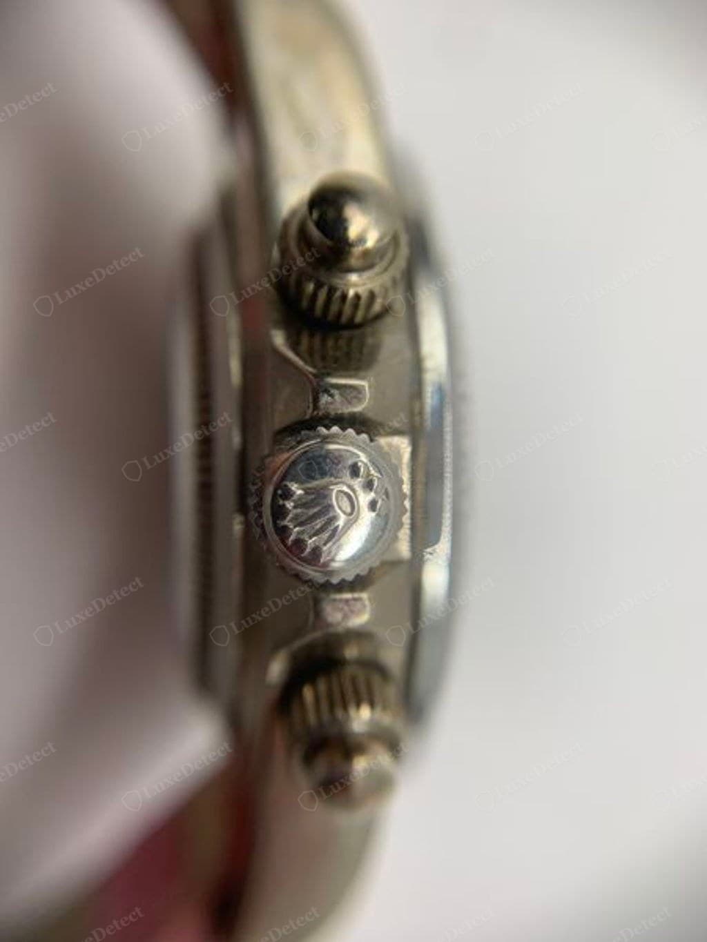 Winding crown on a counterfeit Rolex Daytona-style watch — a close-up (slightly out of focus) showing a shallow-looking coronet with several dots scattered around it rather than a clean marking beneath the coronet