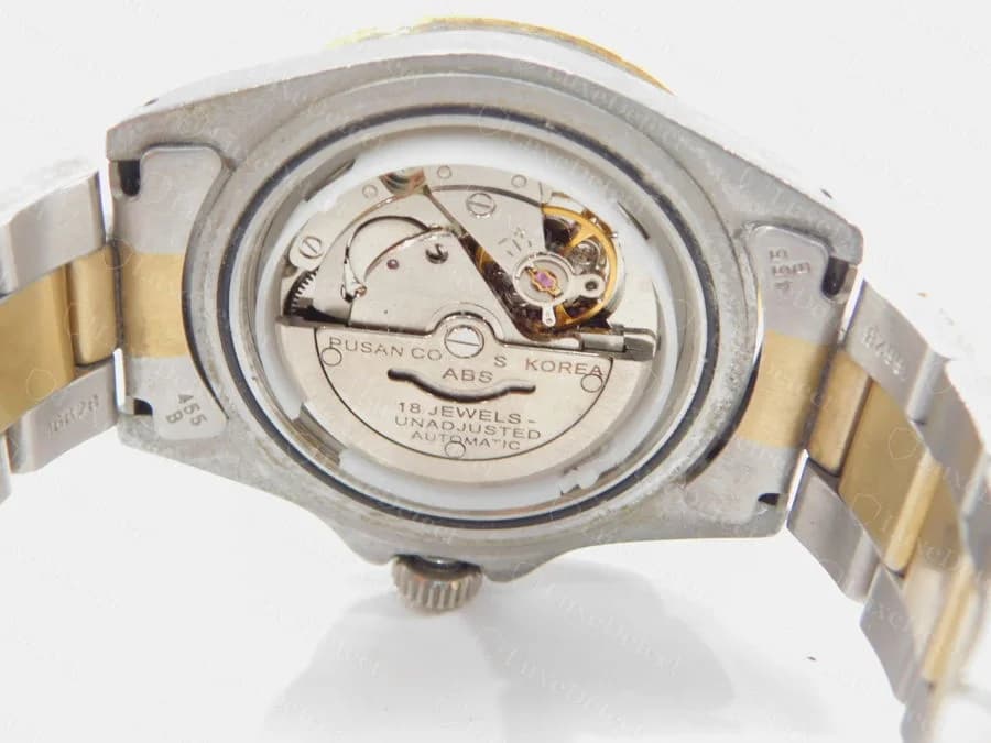 Movimiento de un Rolex falso visto con el fondo de caja abierto: una platina genérica de producción masiva con las inscripciones "Pusan Co S Korea", "ABS", "18 Jewels", "Unadjusted", "Automatic", nada que se parezca a un calibre Rolex