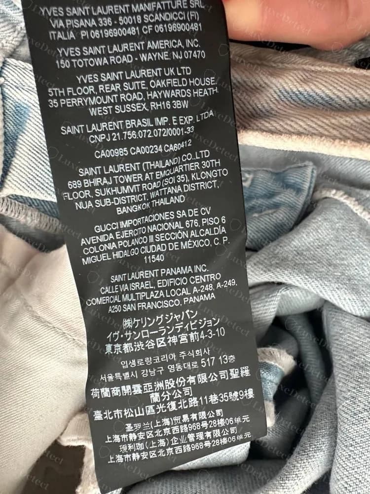Etiqueta legal genuina con varias empresas, que enumera importadores y distribuidores por mercado, en texto latino, japonés, coreano y chino, en el interior de una prenda de denim claro.