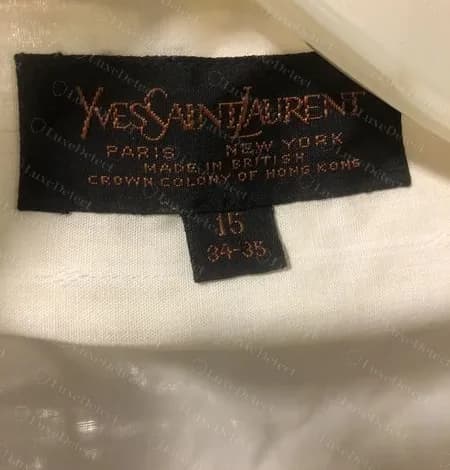 Etiqueta negra genuina Paris New York con letras cobre y un bloque de talla que dice 15, 34-35, en el interior del cuello de una camisa blanca, con la línea de fabricación que dice British Crown Colony of Hong Kong.