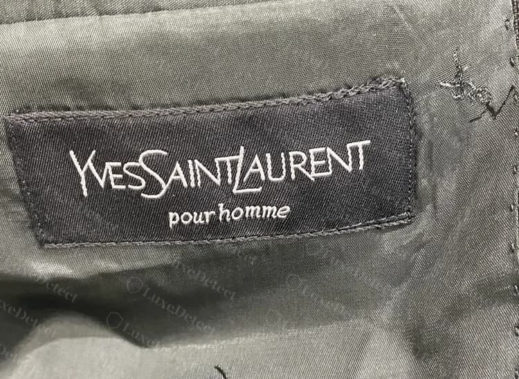 Genuine pour homme label in white on black, sewn into the lining of a suit jacket, with the same wordmark and script "pour homme" as the cream version.