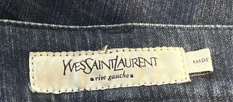 Étiquette rive gauche authentique cousue à l'intérieur de la ceinture d'un jean foncé, avec le début de la bande de fabrication visible à droite.