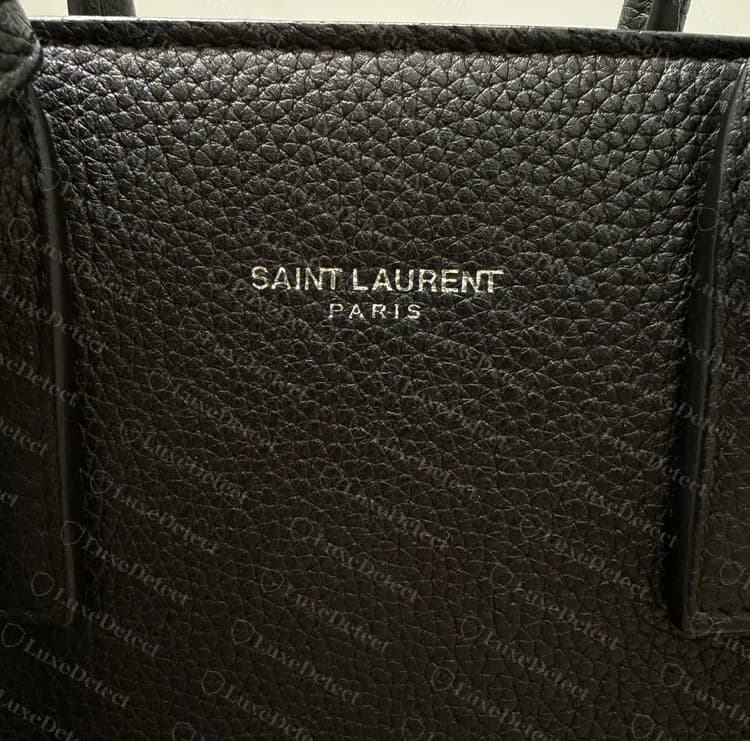 Sello frontal de un Sac de Jour genuino: SAINT LAURENT sobre un PARIS más pequeño y muy espaciado, en foil plateado prensado en el cuero granulado
