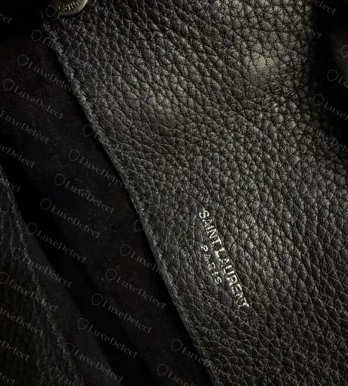 Interior de un Sac de Jour genuino: SAINT LAURENT PARIS estampado en la pared interior de cuero, con el broche lateral arriba y el forro de ante negro debajo