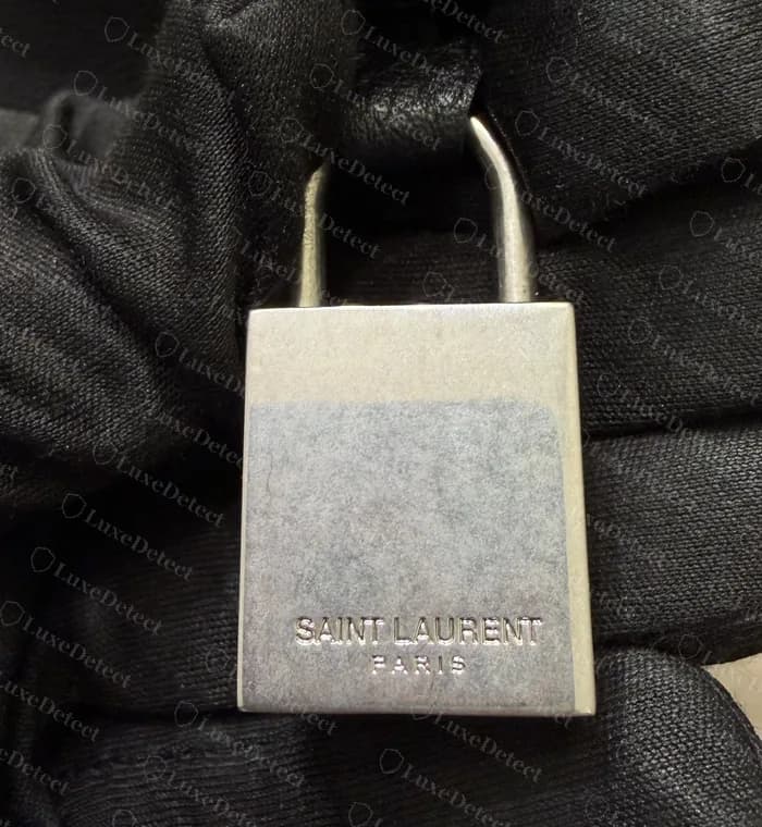 Genuine Sac de Jour padlock: a solid squared block in brushed silver, SAINT LAURENT over PARIS stamped low on the face
