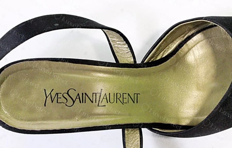 Genuine gold cursive "Yves Saint Laurent" script logo stamped into the gold-tone insole of a black satin evening sandal.