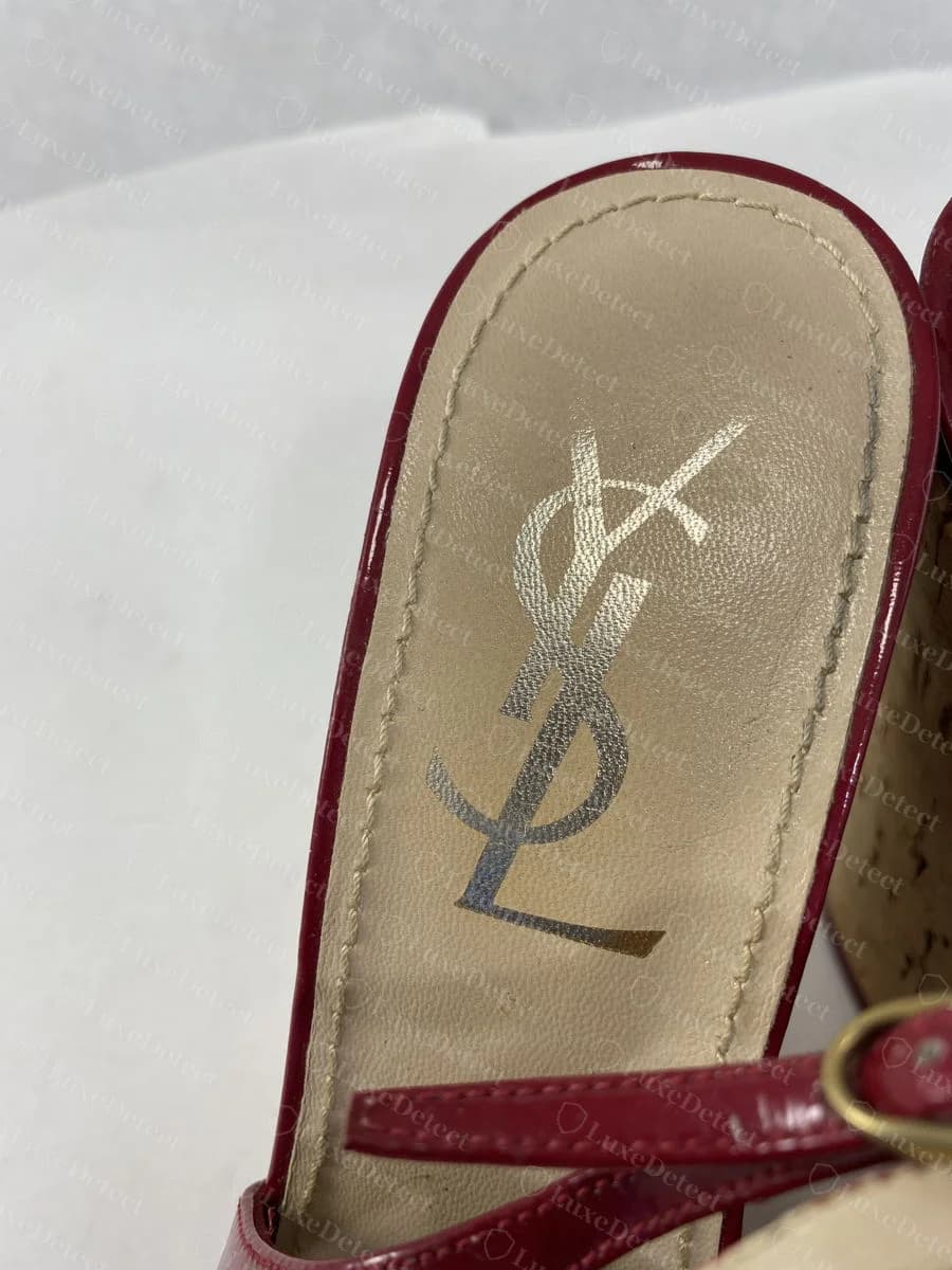 Genuine gold-foil printed "YSL" monogram on the insole of a red patent wedge sandal, a related but visually distinct print treatment from the bootie above.