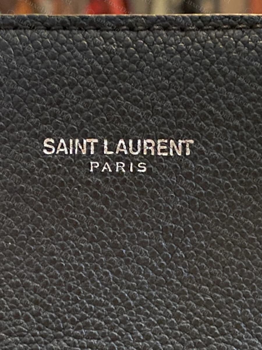 Genuine "SAINT LAURENT PARIS" logo plate on the front panel, crisp and level above the handles.