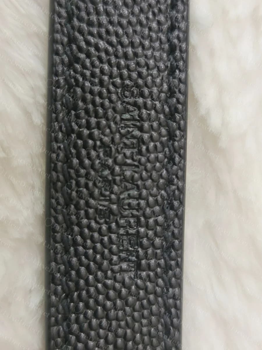 Counterfeit Saint Laurent Envelope strap leather emboss, the "SAINT LAURENT" text garbled and running the wrong direction, not a clean single line