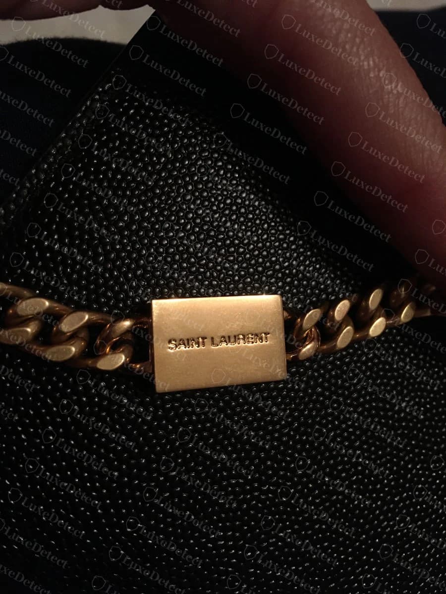 Saint Laurent Kate chain-bar plaque held in hand, showing the engraved SAINT LAURENT text and the weight of the curb-link chain