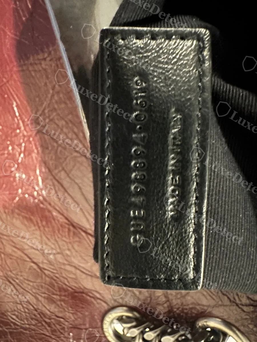 Counterfeit Saint Laurent Niki date code tab reading "GUE498894-0619" and "MADE IN ITALY," stamped at a rotated angle relative to the tab