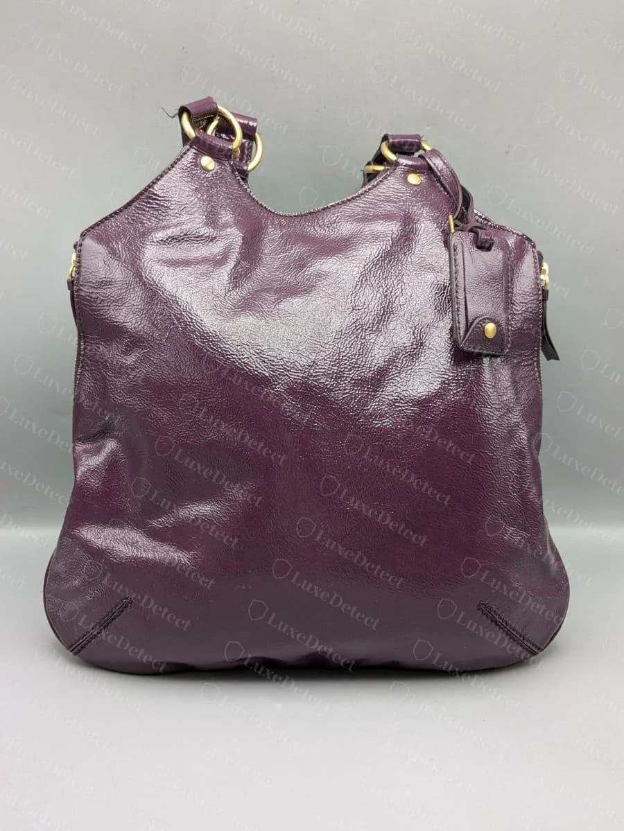 A second, aubergine-colored Tribute Tote shows the same hardware, labeling, and construction as the black version.