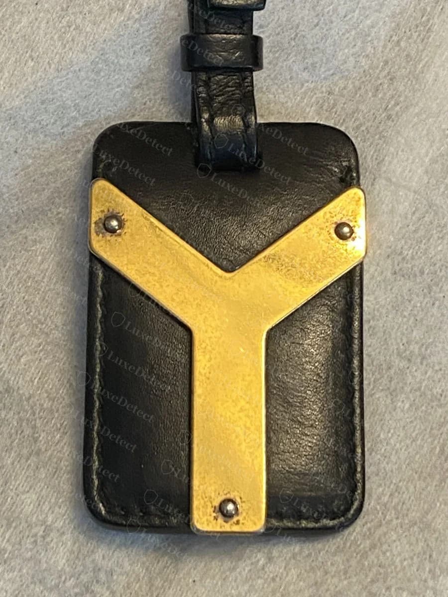The Y-shaped brass plaque hangs from a leather tab on the shoulder strap ring, secured with three visible rivets.