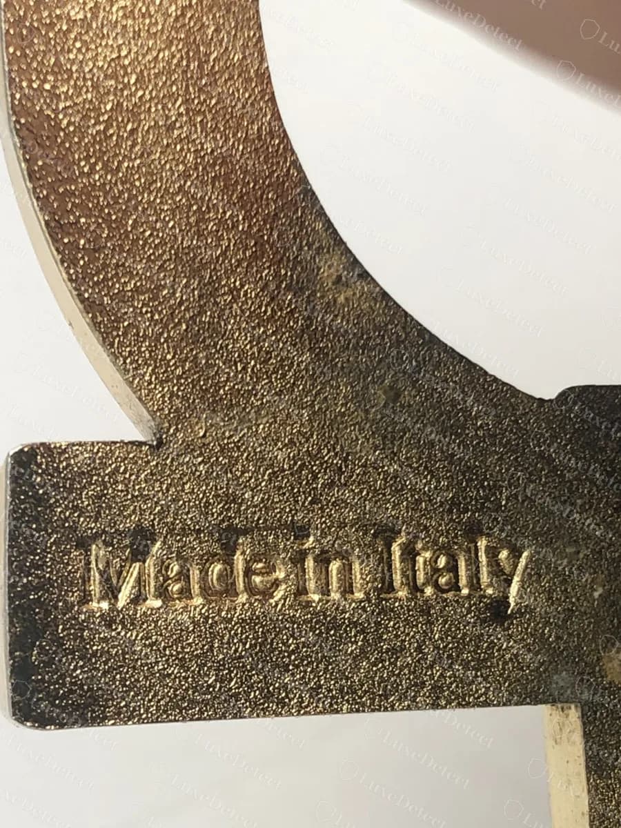Back of a genuine one-piece Gancini buckle: "Made in Italy" in raised script on the centre bar, against a sandblasted gold-tone surface