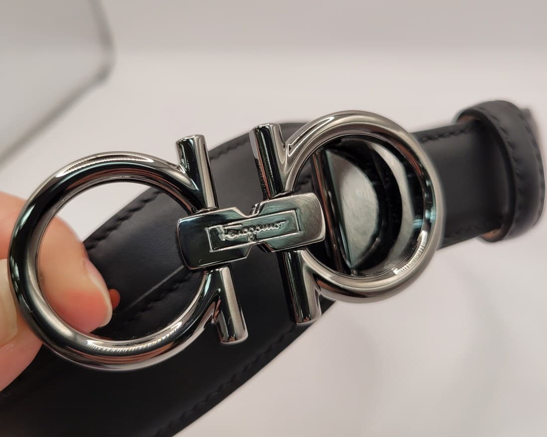 Counterfeit Salvatore Ferragamo Gancini buckle — the same double-ring silhouette but in uniform mirror-polished metal with no ribbed texture anywhere on the frame, only the "Ferragamo" script plate breaking up the smooth surface