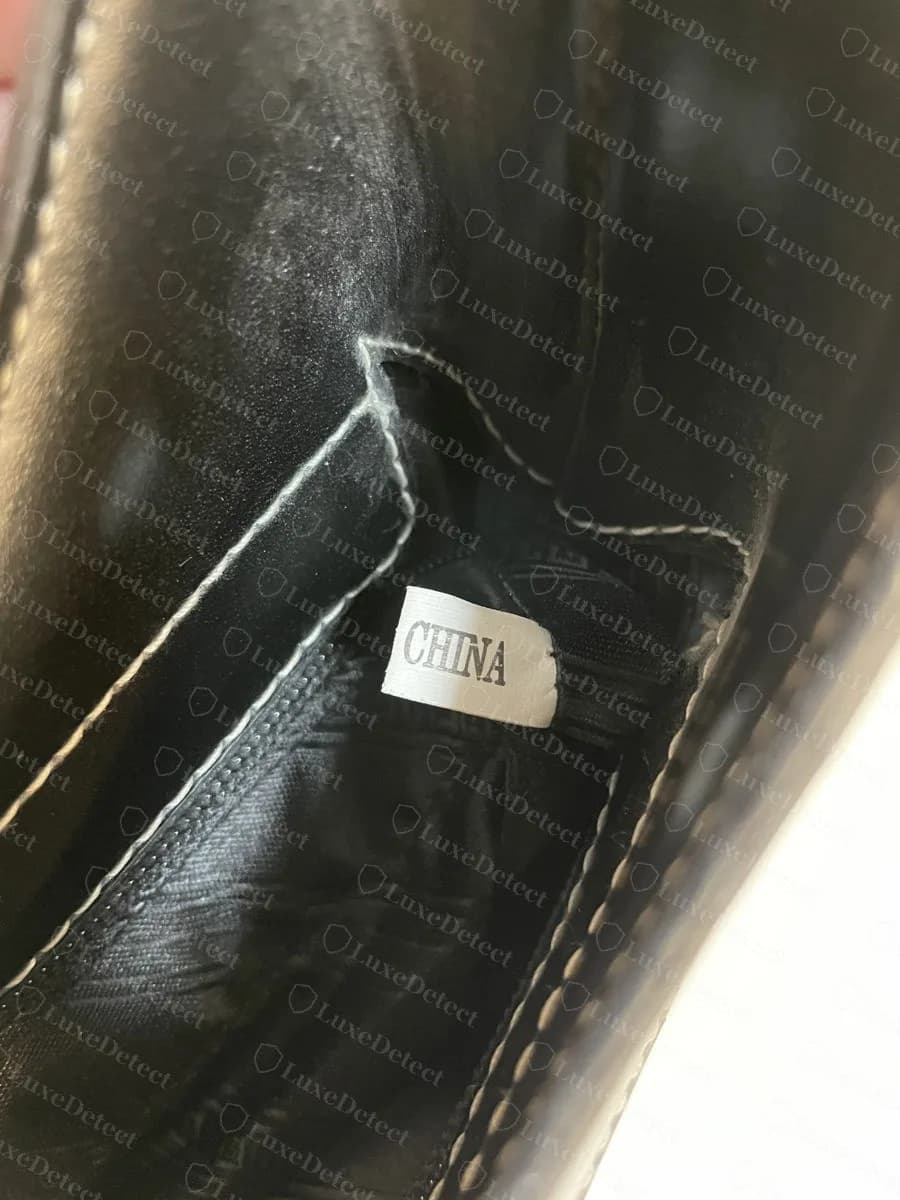 Una etiqueta blanca cosida con el texto CHINA dentro de un bolso Ferragamo falsificado, en lugar de una línea estampada de Made in Italy