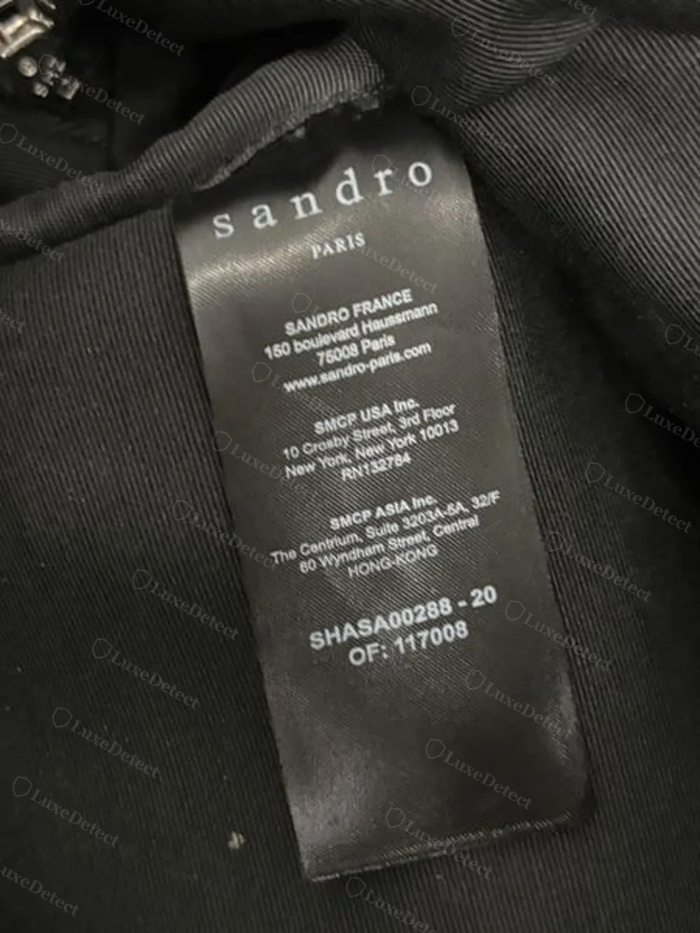 SMCP corporate address label sewn inside the main compartment of Sandro's nylon book bag, listing SANDRO FRANCE, SMCP USA Inc., and SMCP Asia Inc. addresses.