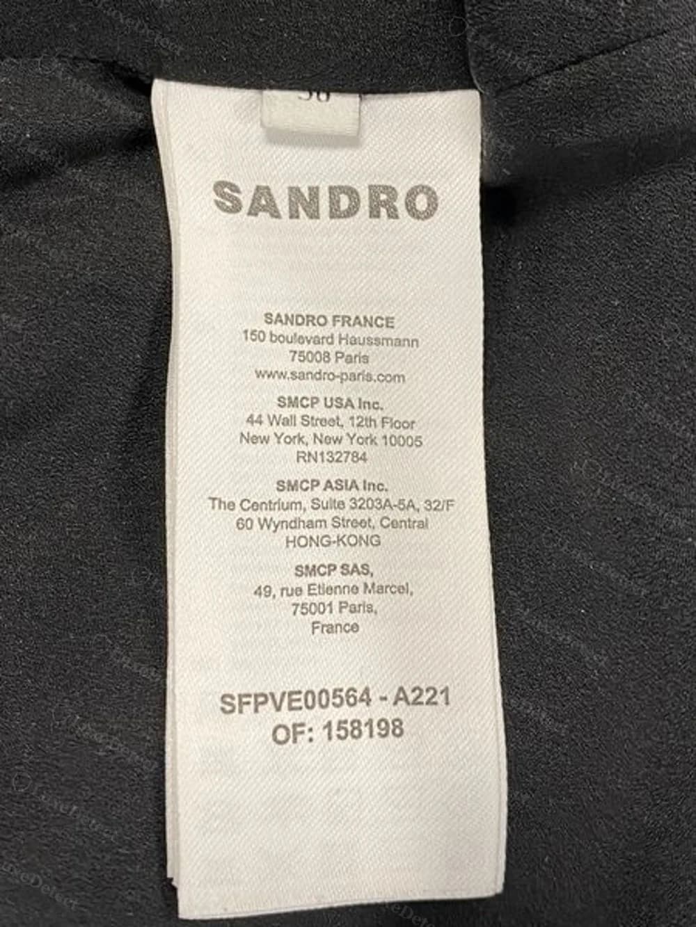 Woven "SANDRO" wordmark and SMCP corporate address label together on one tag, sewn at the interior collar seam of a cropped tweed jacket.
