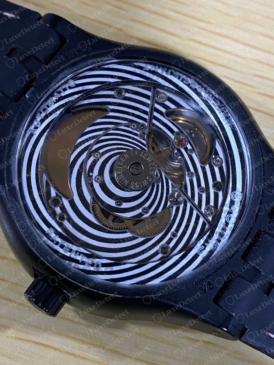 Genuine Swatch Sistem51 automatic movement seen through a transparent case back printed with a black and white spiral, a ring reading NINETEEN 19 JEWELS SWISS, and AUTOMATIC and PATENTED around the edge