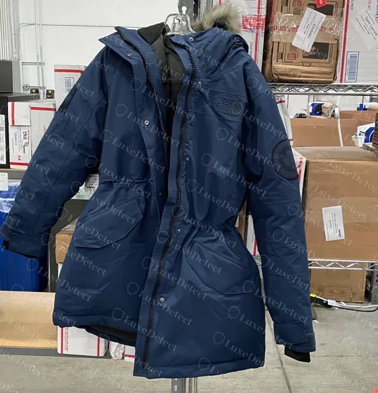 Una parka de plumas North Face genuina con capucha de pelo sintético, un parche redondo en la manga y dos grandes bolsillos delanteros