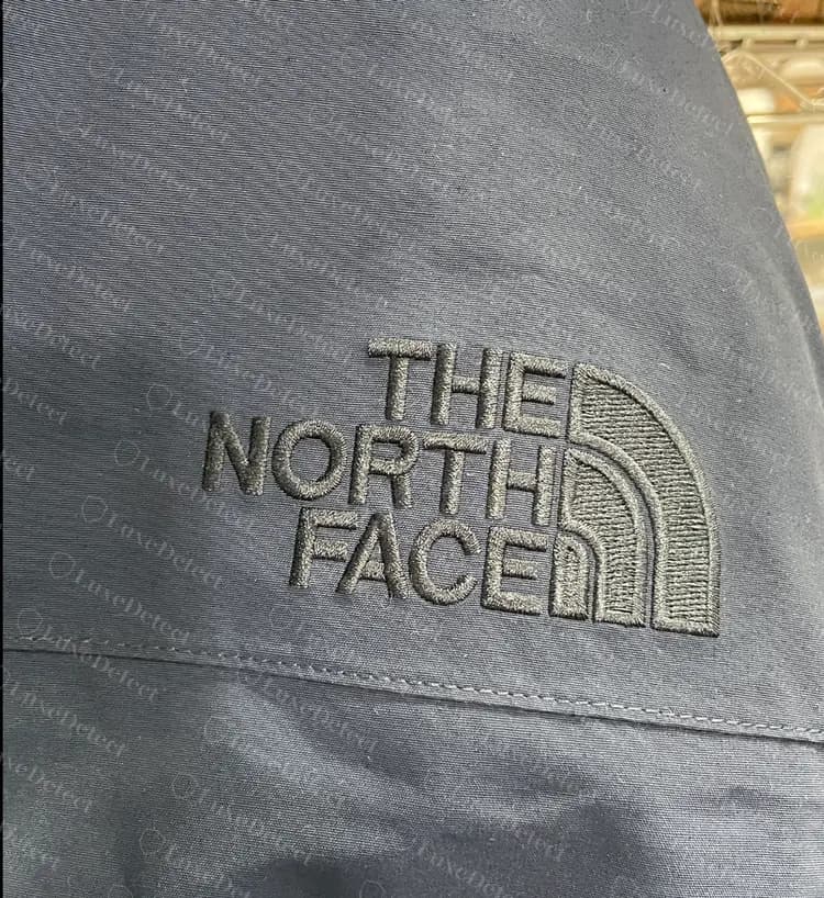 Genuine tonal embroidered logo on a down parka sleeve: tightly stitched dome segments and sharp lettering