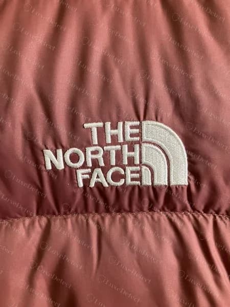 Genuine white embroidered chest logo on a mauve women's puffer, with an even satin stitch and no gaps in the dome