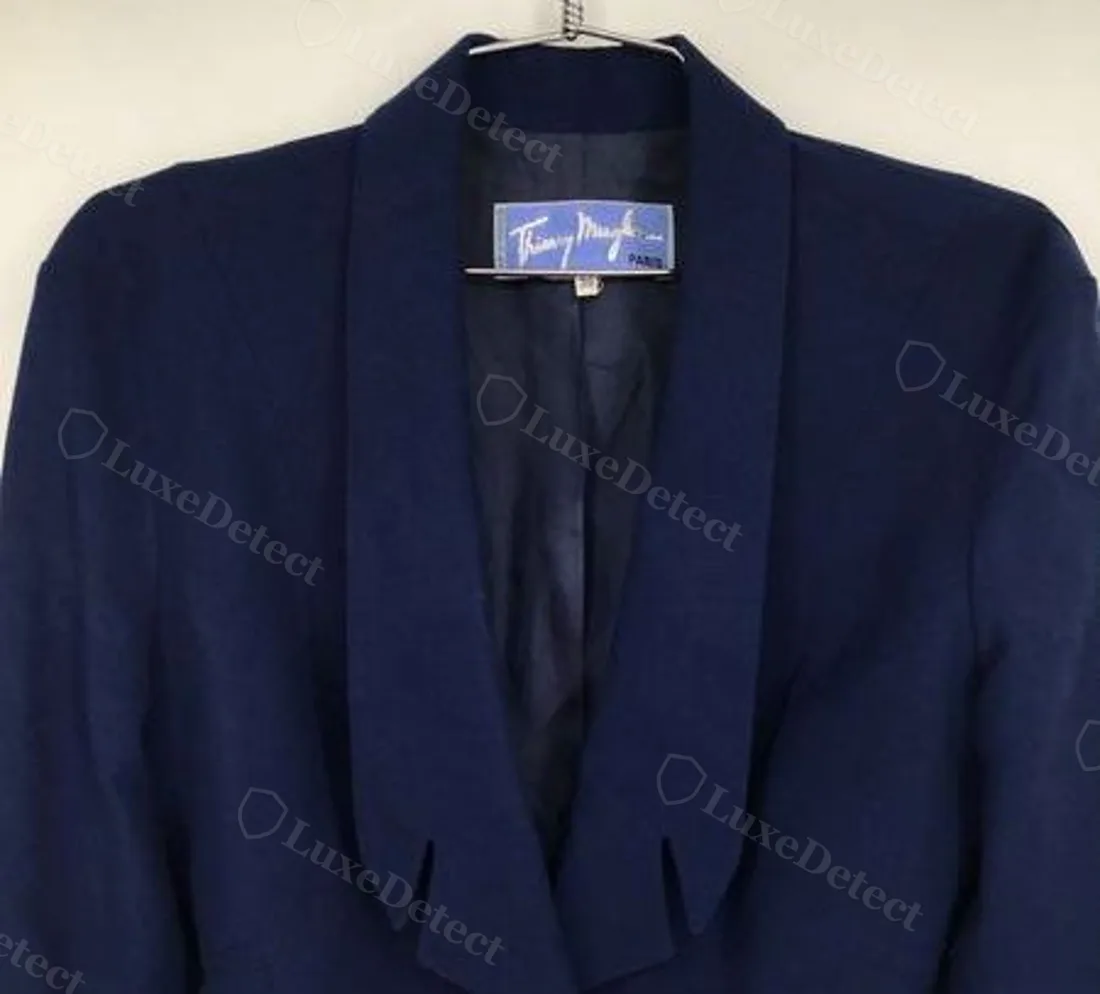 Authentic Thierry Mugler interior label on a navy blazer: cobalt satin ribbon, sewn at the top edge only, signature in bright silver-white thread, hanging free at the bottom.